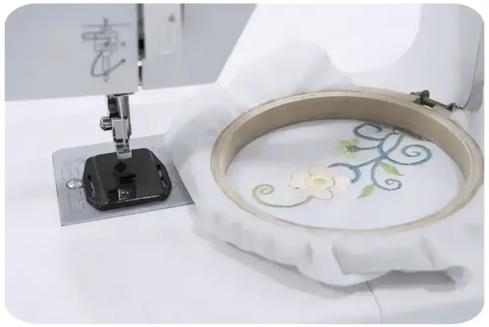 Tissu blanc tendu dans un cercle à broder en bois avec motif floral brodé crème et vert machine à coudre 900-V