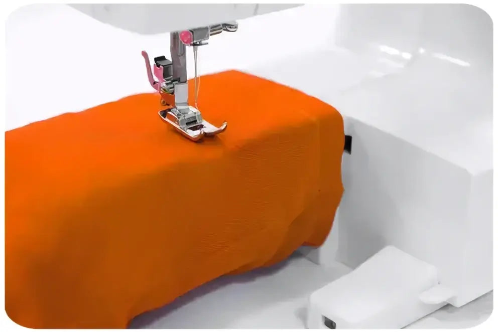 Machine à coudre 900-V en train de coudre un tissu orange sur une machine blanche pour travaux de couture